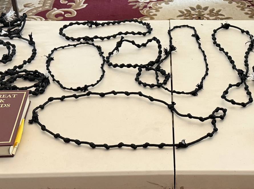 Table with black prayer ropes, scissors, and The Great Book of Needs placed on a decorative surface