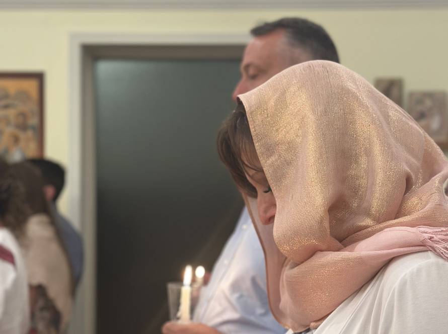 Woman in pink headscarf holding candle during religious ceremony indoors