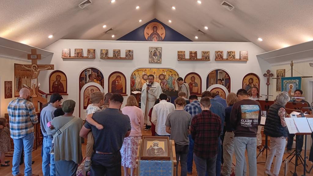 Congregation in an Orthodox church service with icons and priest conducting liturgy amidst worshippers