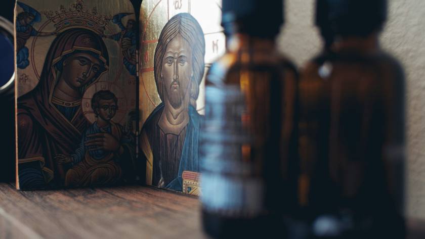 Religious icons beside glass bottles on wooden shelf, serene atmosphere, spiritual decor, home altar setup