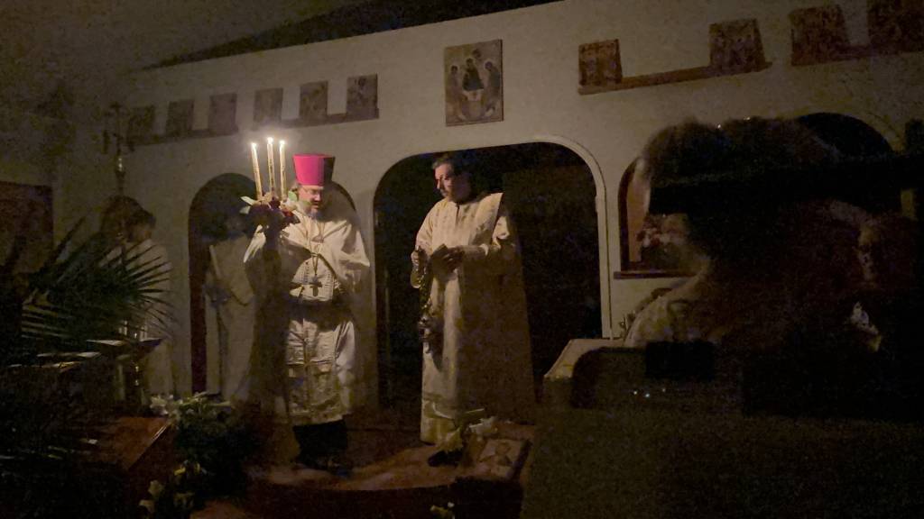 Orthodox church service with priest holding candles during evening ceremony