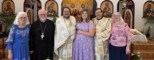 Group posing in a church with icons and flowers in the background, people in ceremonial attire and colorful outfits