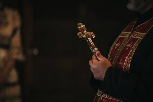 Priest holding ornate cross during church service, wearing traditional religious garments
