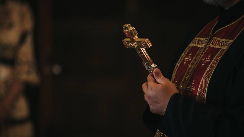 Priest holding ornate cross during church service, wearing traditional religious garments