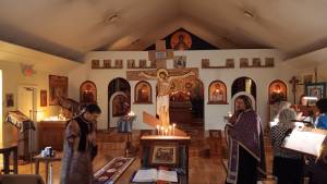 Orthodox church interior with icons, cross, and candles during a service with clergy and congregation members.