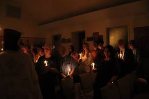 People gathered in a dim room holding candles during a solemn candlelit ceremony, creating a warm, serene atmosphere