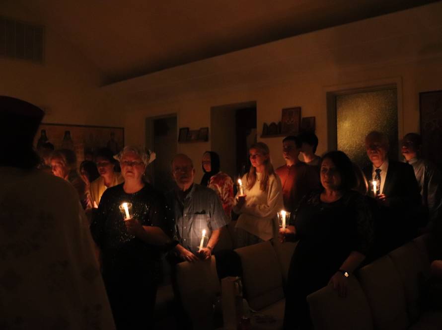 People gathered in a dim room holding candles during a solemn candlelit ceremony, creating a warm, serene atmosphere