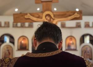 Priest standing in front of ornate church altar with large crucifix in background