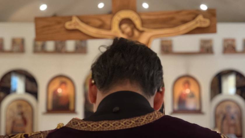 Priest standing in front of ornate church altar with large crucifix in background