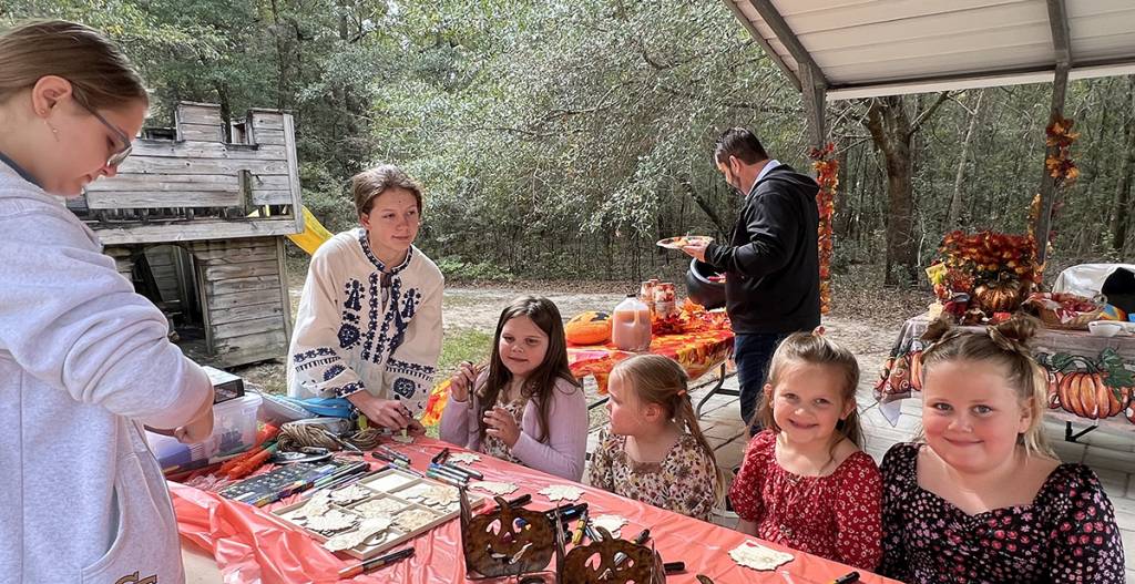 Children and adults enjoying a festive outdoor craft activity at a fall-themed party setup with pumpkins and decorations