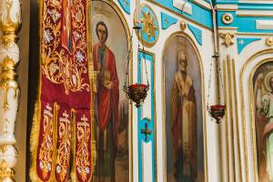 Ornate church interior featuring religious icons, intricate red textiles, and decorative hanging lamps in vibrant colors