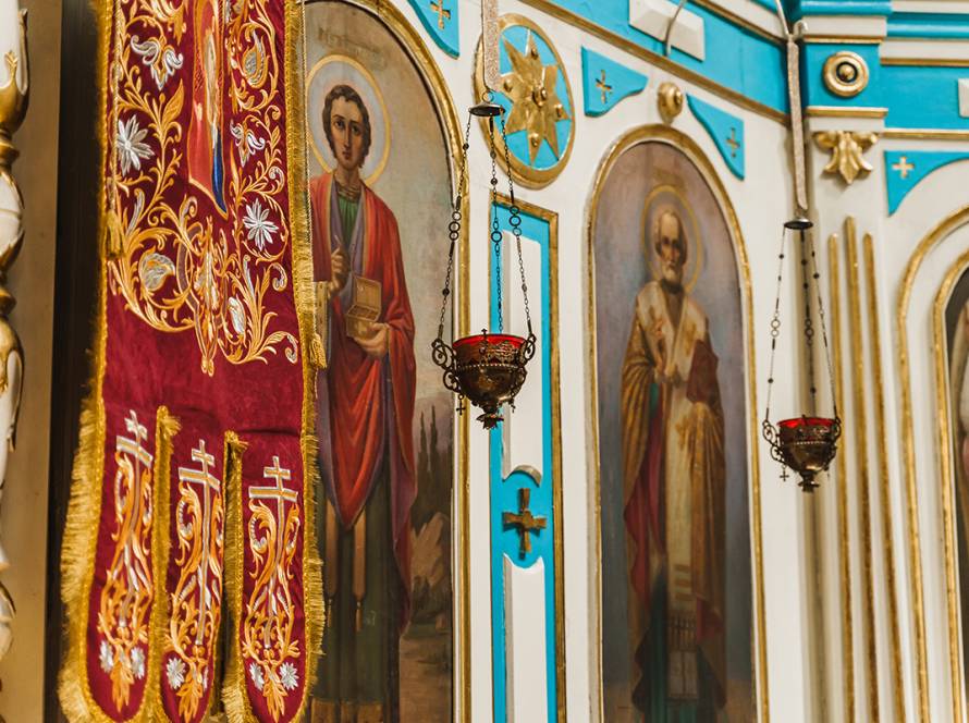 Ornate church interior featuring religious icons, intricate red textiles, and decorative hanging lamps in vibrant colors