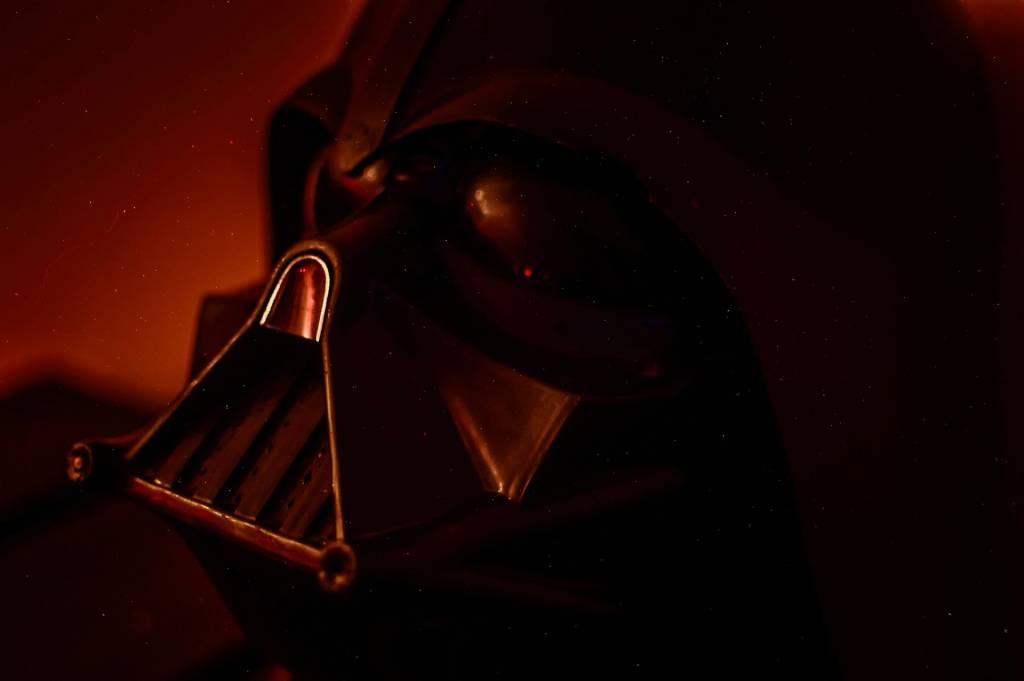 Close-up of a dark, futuristic helmet with red lighting and textured surface.