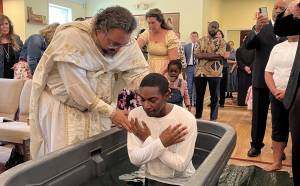 Priest performing baptism ceremony for a man in front of a congregation inside a church setting, people observing