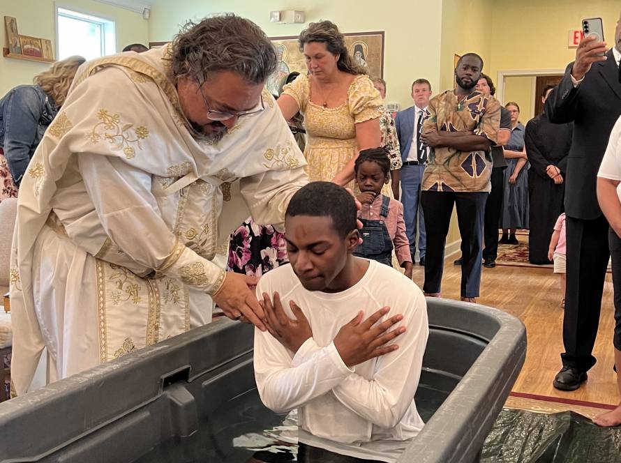 Priest performing baptism ceremony for a man in front of a congregation inside a church setting, people observing