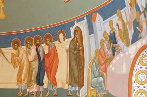 Religious mural depicting apostles with halos in vibrant robes engaged in a gathering indoors
