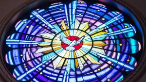 Colorful stained glass window with a white dove at the center, radiating blue and yellow light patterns