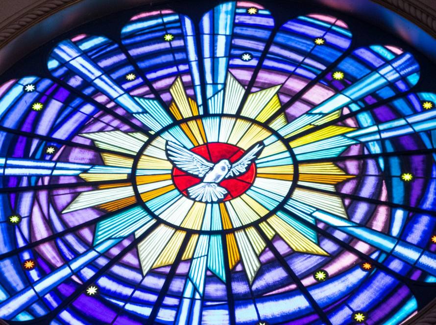 Colorful stained glass window with a white dove at the center, radiating blue and yellow light patterns