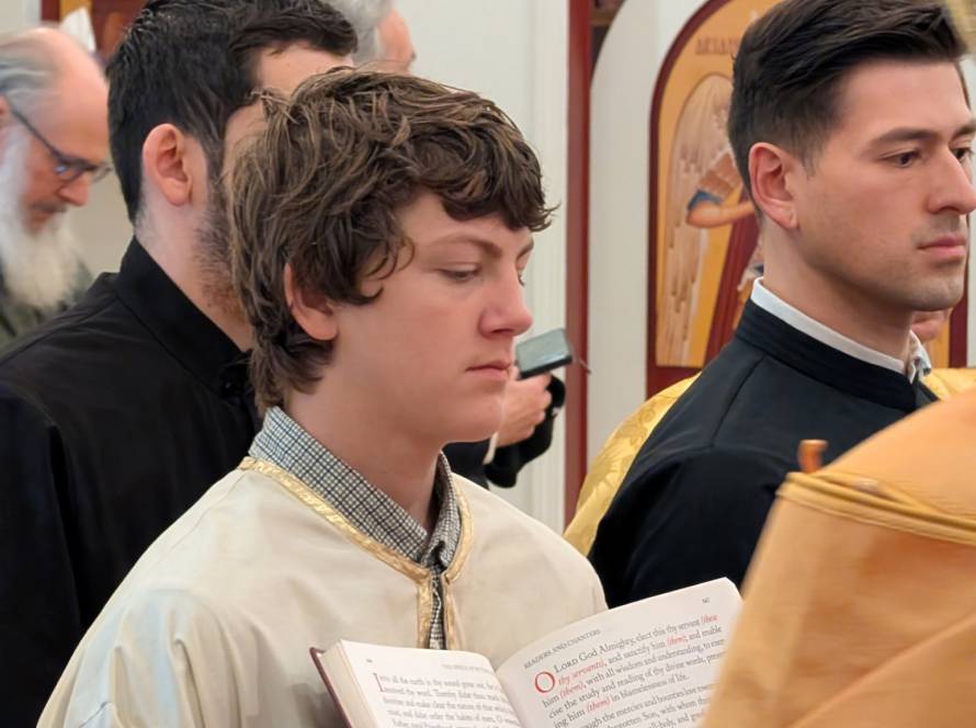 Young men participating in a religious ceremony, holding a book with text, wearing traditional garments in a decorated setting