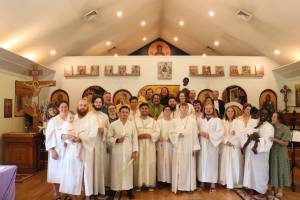 Group of people in white robes holding candles and palm branches inside a church with religious icons