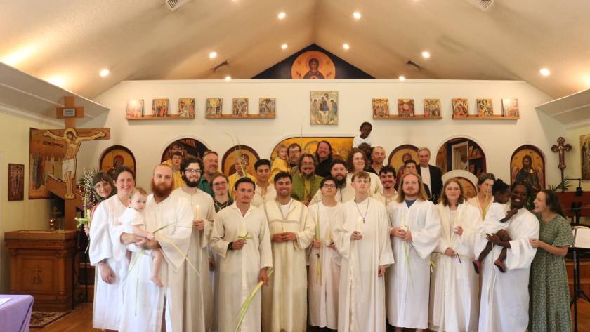 Group of people in white robes holding candles and palm branches inside a church with religious icons