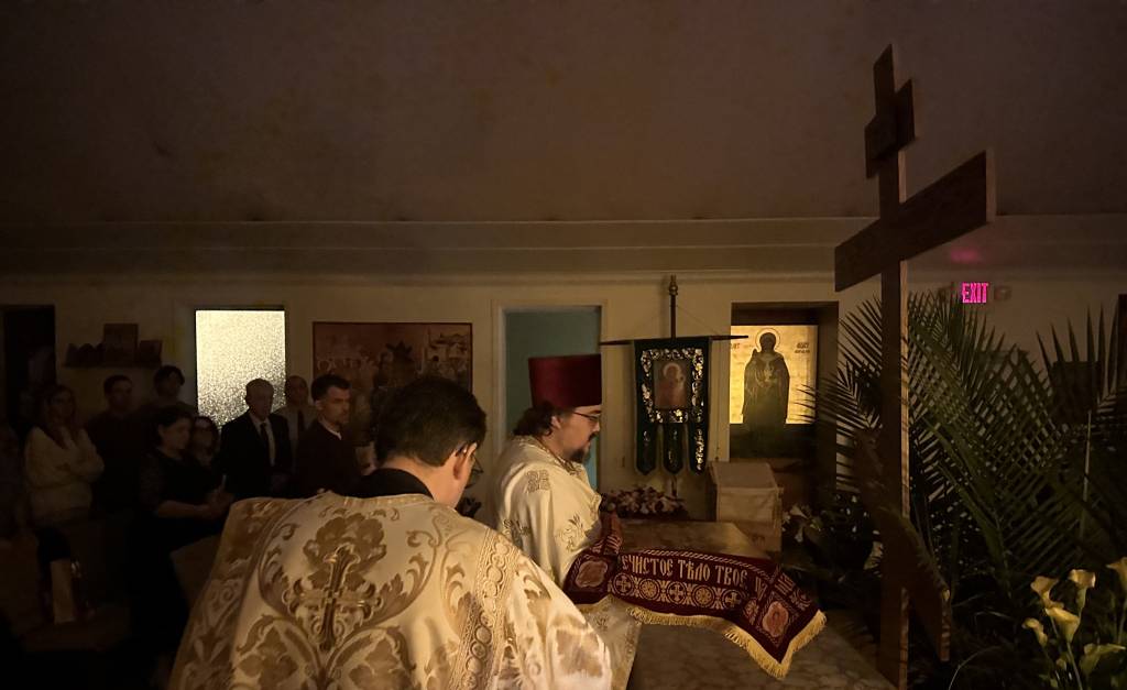 Orthodox Christian service with clergy and congregation in dimly lit church, adorned with icons and religious symbols