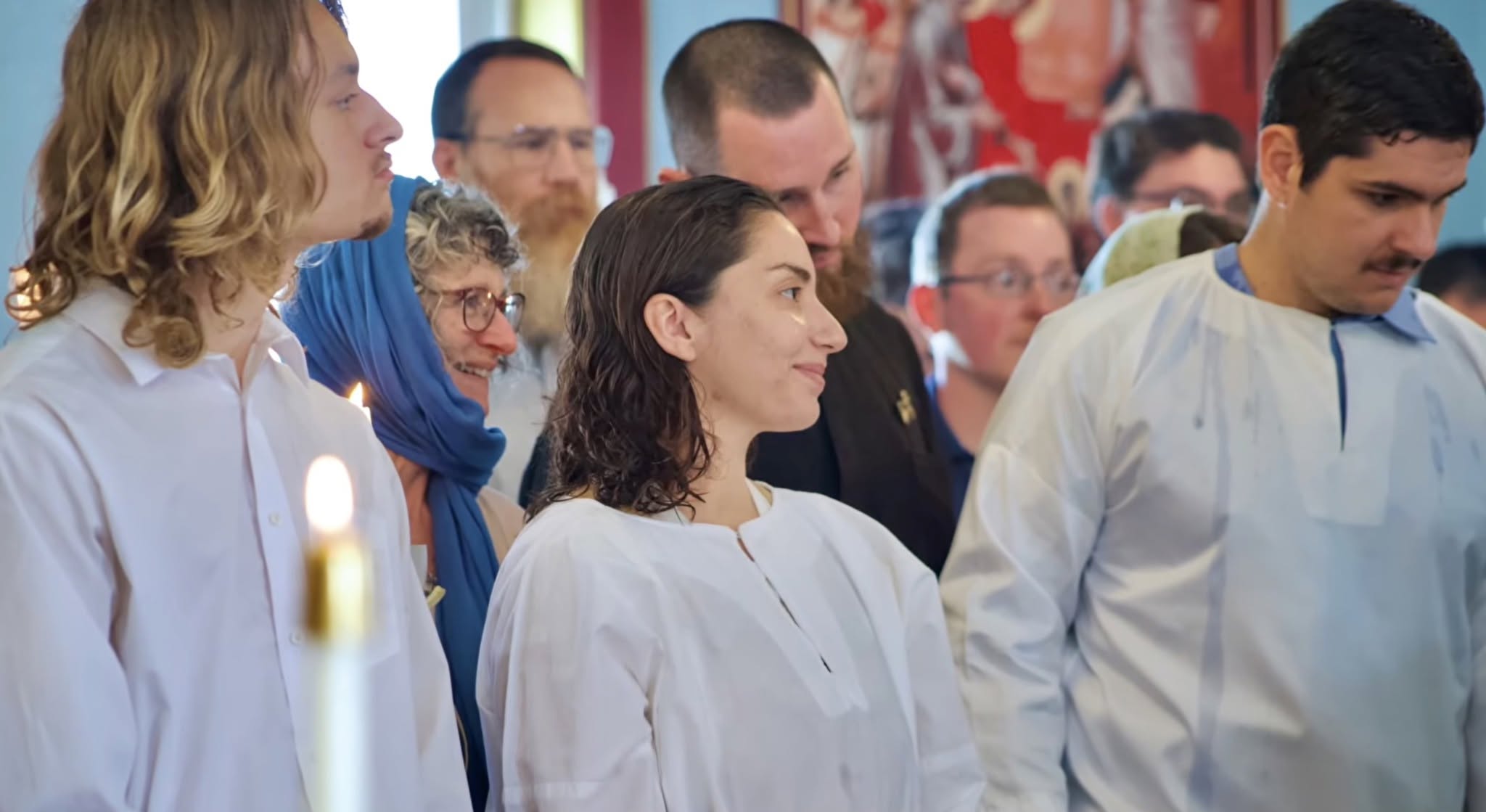 Group of people wearing white garments participating in a ceremonial gathering with candles and attentive expressions