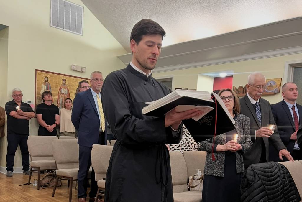 Reader reading from a book during a candlelight church service with attendees standing in the background