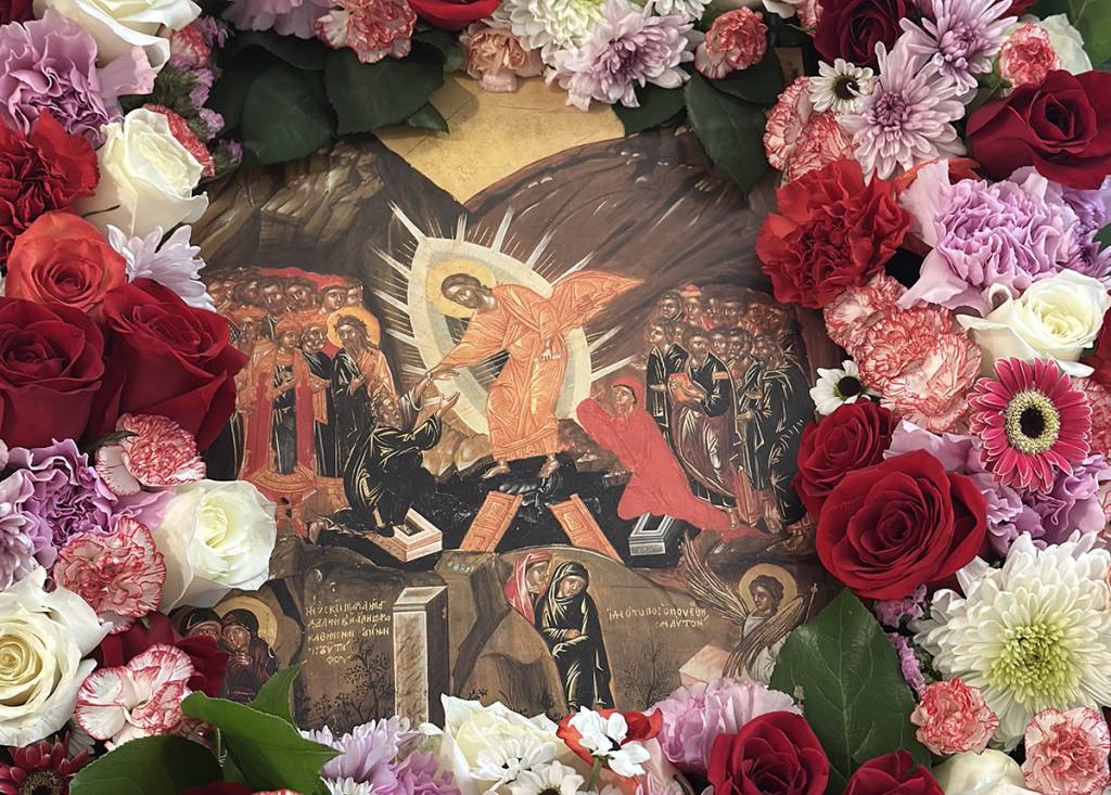 Religious icon surrounded by vibrant flowers including roses and carnations, depicting a sacred biblical scene