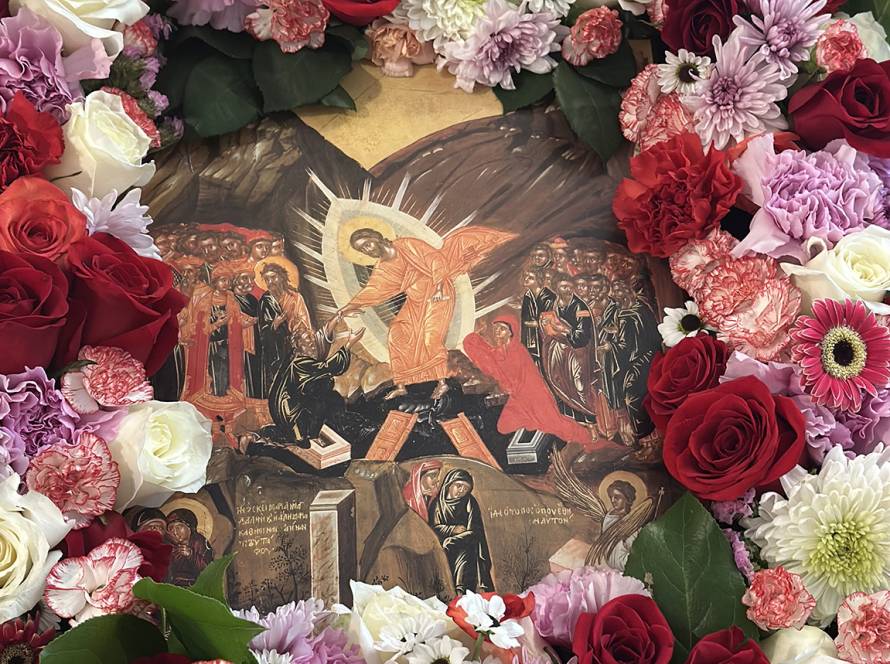 Religious icon surrounded by vibrant flowers including roses and carnations, depicting a sacred biblical scene