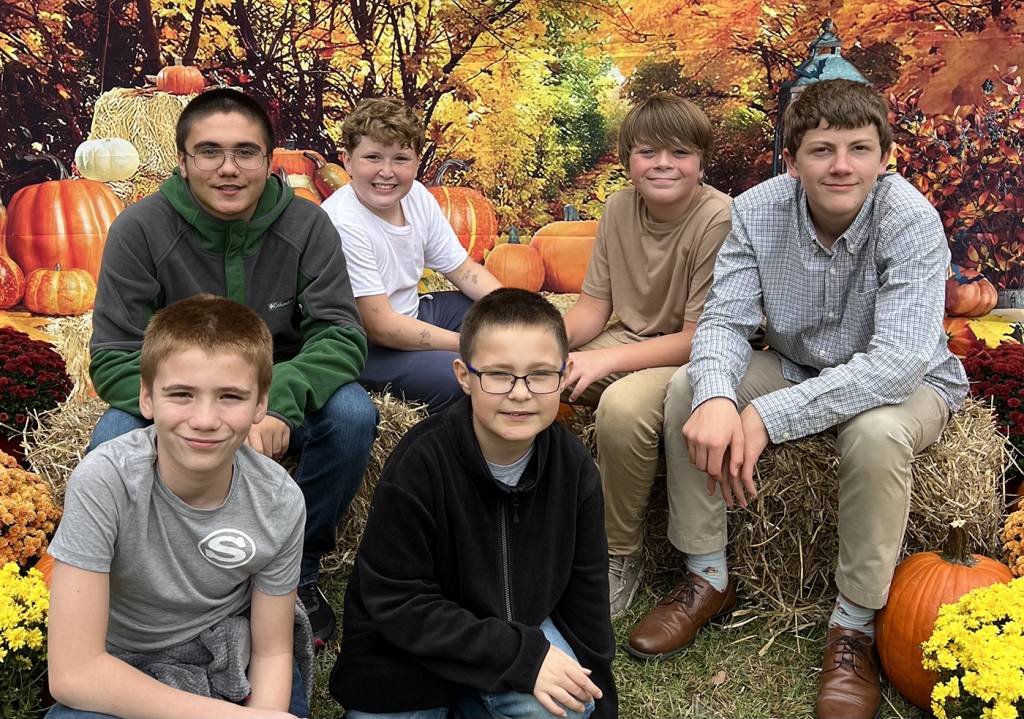 Group of boys sitting on hay bales with pumpkins and autumn leaves background at a fall festival