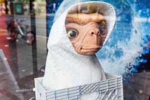 Alien figurine in white blanket inside a basket with a cosmic backdrop and reflections in a window display