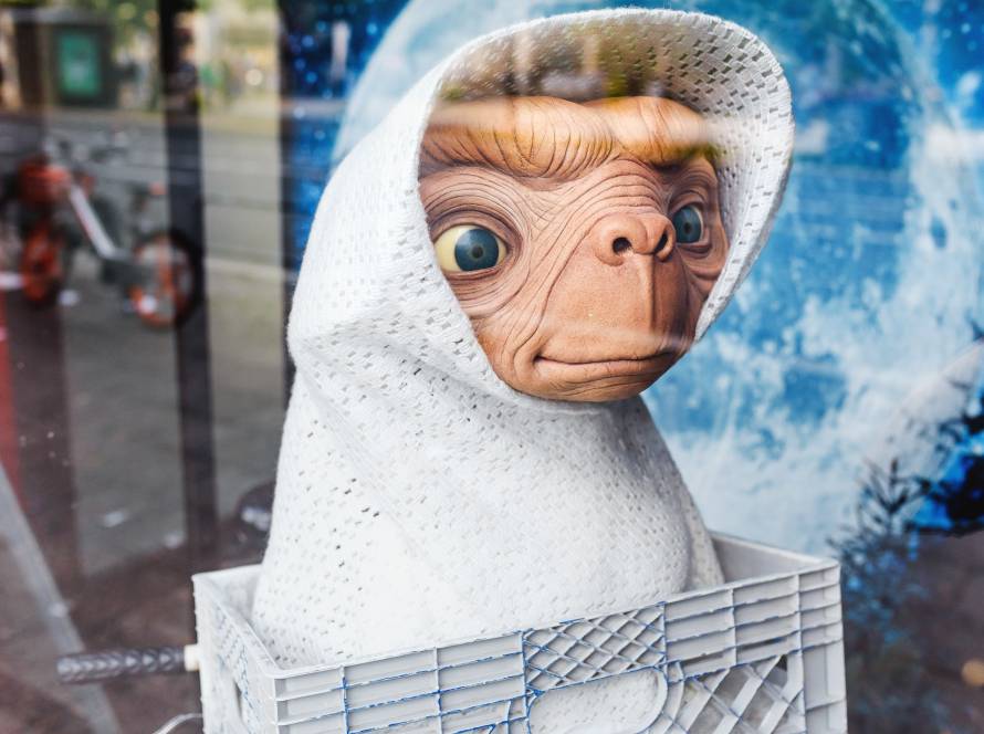 Alien figurine in white blanket inside a basket with a cosmic backdrop and reflections in a window display