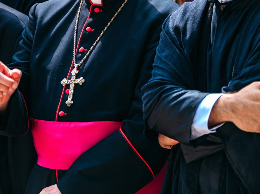 Clergy members in religious attire, showcasing a cross necklace and vibrant sash during a ceremonial event.