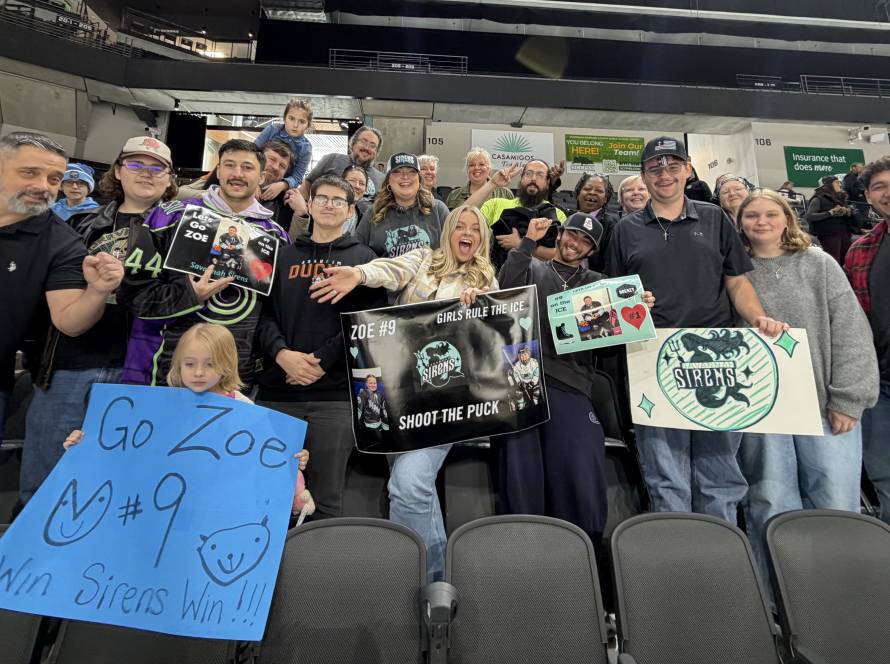 Group of enthusiastic hockey fans at a game holding supportive signs for Zoe and the Sirens team