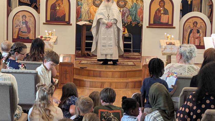Orthodox priest leading service with diverse congregation in church with iconography and lit candles
