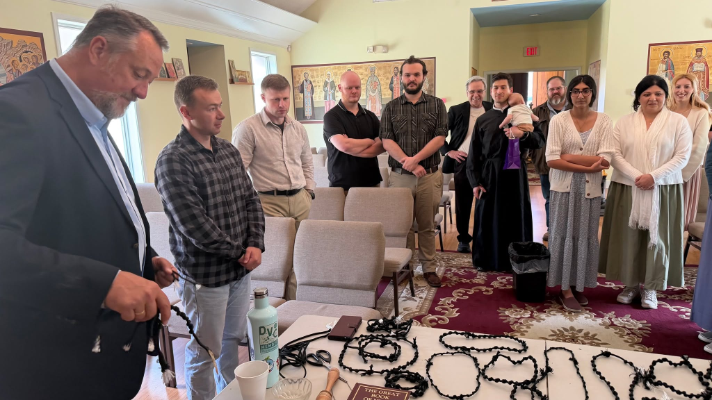 Group gathered in a room with icons, observing items on a table at a religious event or ceremony