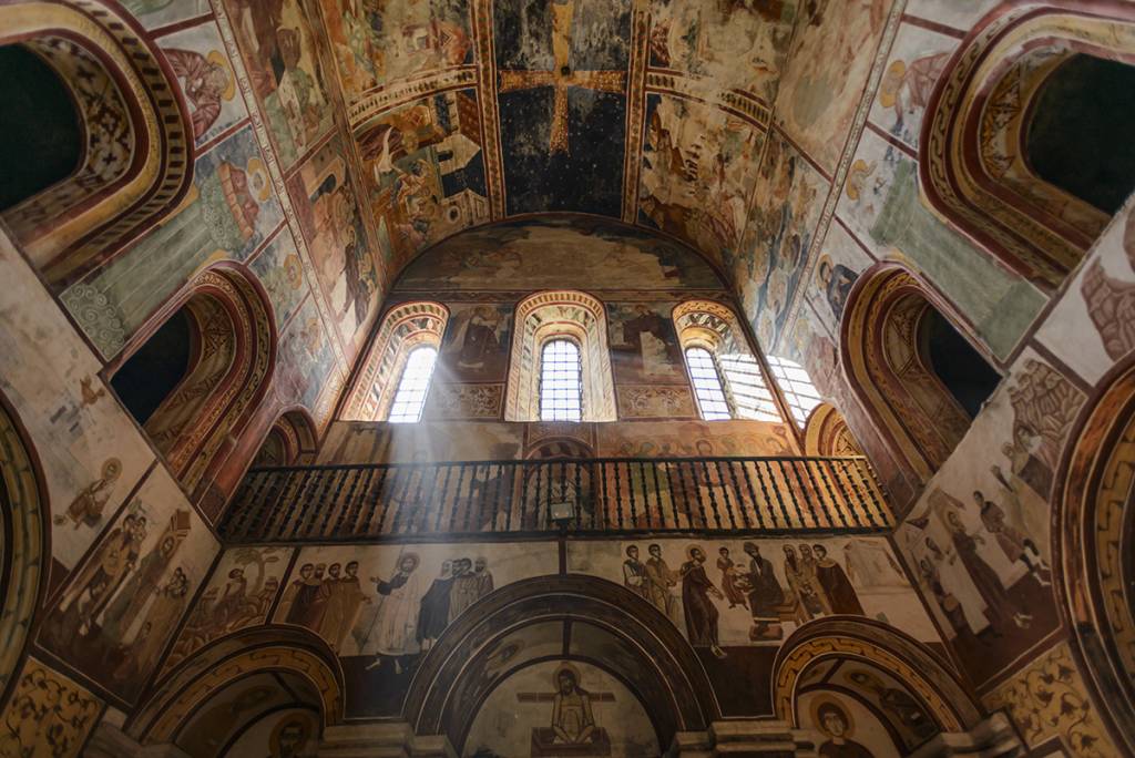 Interior of a historic church with ornate frescoes and arched windows allowing sunlight to stream in
