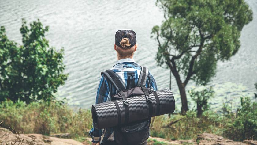 Hiker with backpack and camping mat overlooking serene lake surrounded by trees