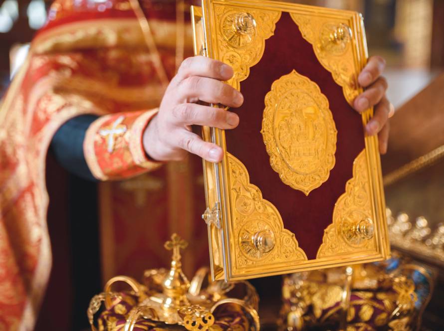 Hands holding ornate religious book with gold details during a ceremony in a church setting