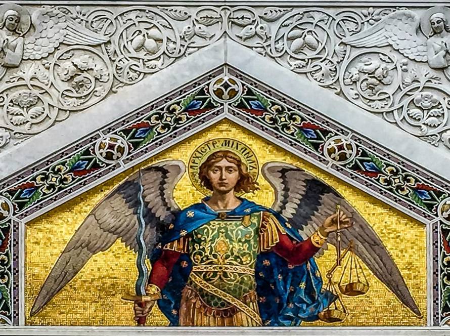 Ornate mosaic of angel with wings, holding sword and scales, surrounded by intricate carvings and celestial motifs