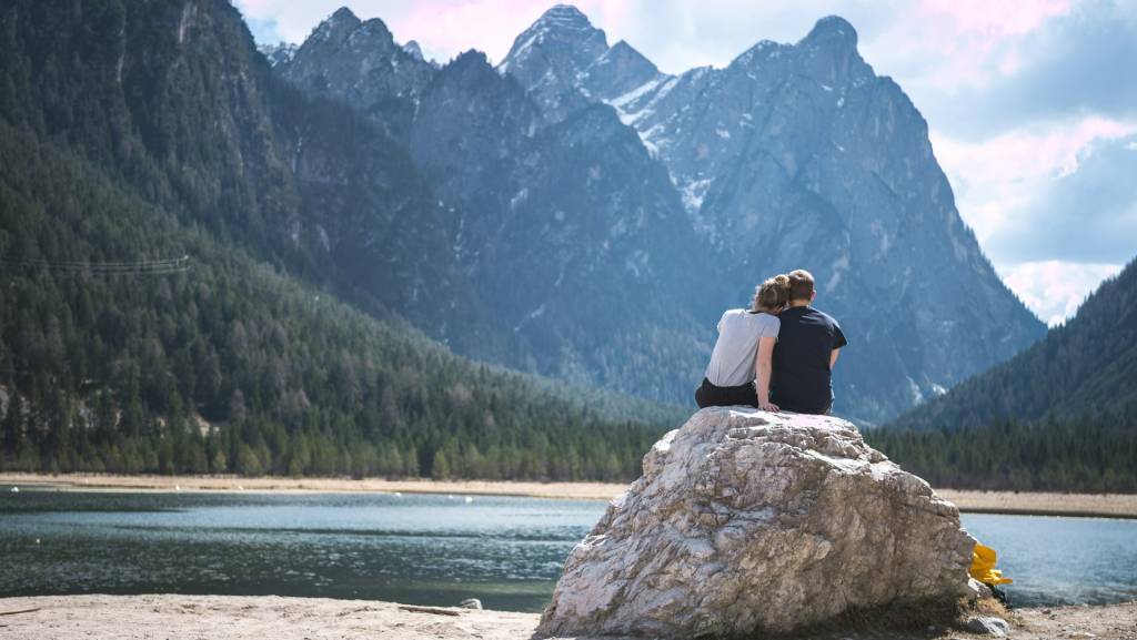 Couple sitting on rock overlooking serene lake with majestic mountain view