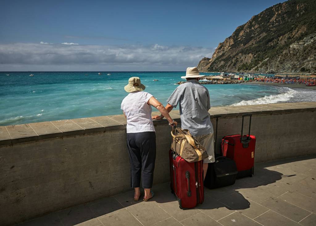 Elderly couple with suitcases enjoy scenic ocean view by the shore, dressed in hats for sun protection