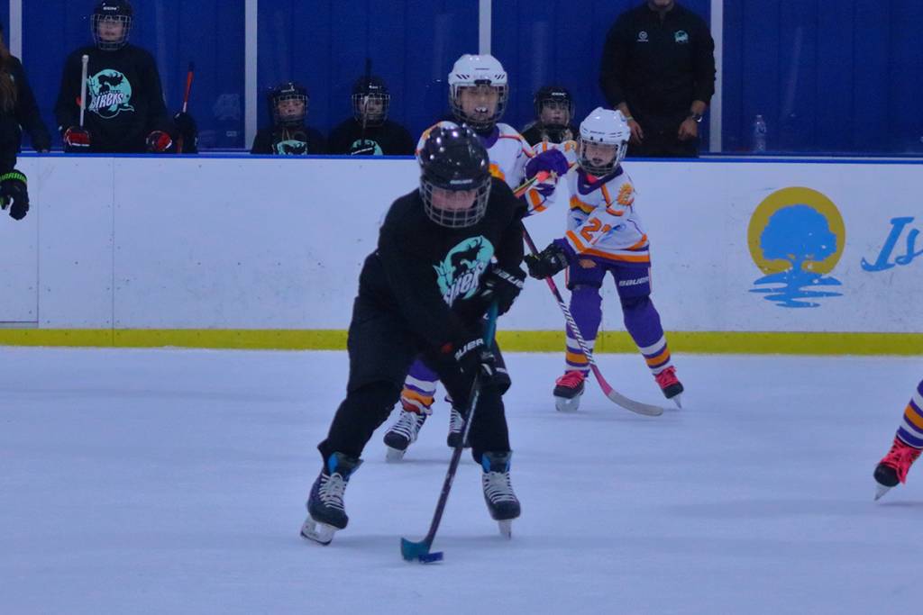 Kids playing ice hockey during a match in a rink, wearing colorful jerseys and helmets, focused on the puck