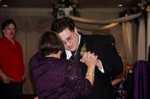 Mother-son dance at a wedding reception, guests in the background, elegantly dressed in formal attire