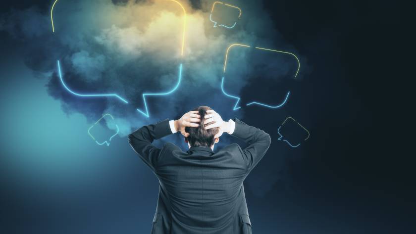 Businessman overwhelmed by glowing speech bubbles in a dark, foggy background, representing communication overload