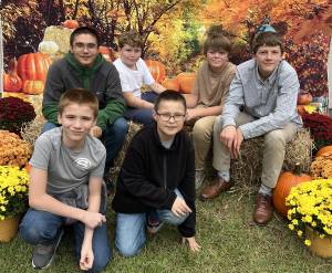 Group of kids sitting on hay bales with autumn foliage and pumpkins in the background at a fall festival
