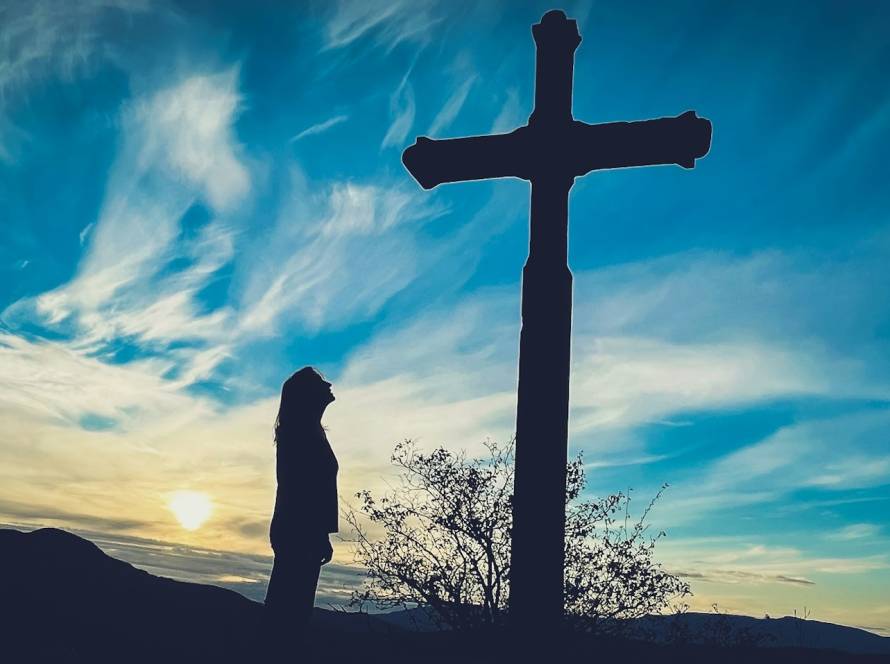 Silhouette of a person standing next to a cross at sunset with a vibrant sky background