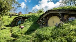 Hobbit-style house with round doors nestled in lush green hills under a blue sky with fluffy clouds