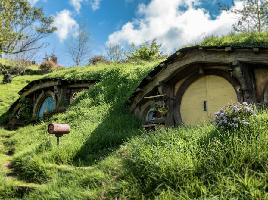 Hobbit-style house with round doors nestled in lush green hills under a blue sky with fluffy clouds